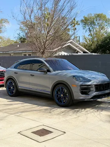 Gray Porsche SUV with blue wheels parked outdoors.