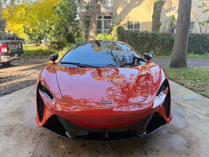 Orange McLaren sports car parked on a paved driveway in front of a house.