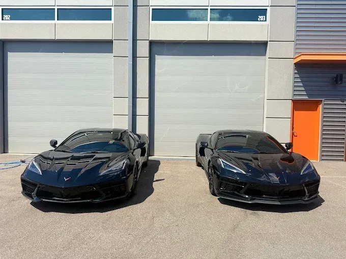 Two black sports cars parked in front of closed garage doors on a sunny day.