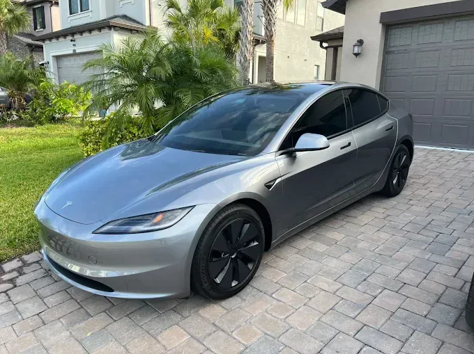 Silver Tesla sedan parked on a brick driveway in front of a house.