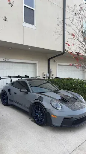 Gray Porsche 911 GT3 RS parked in front of a building with a black hood and spoiler.