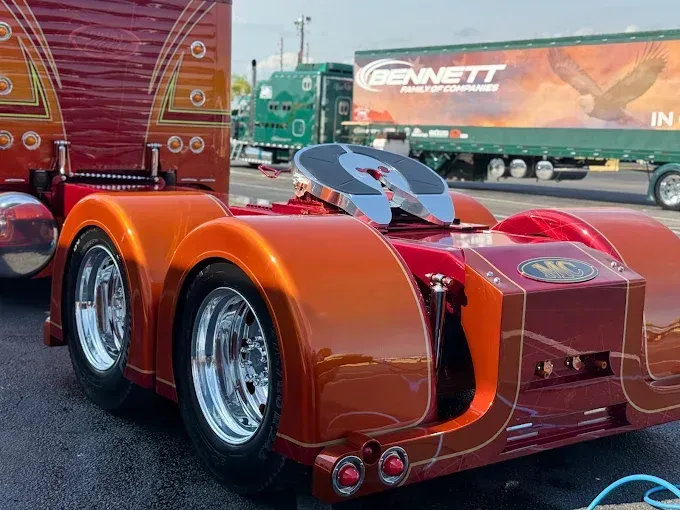 Custom orange semi-truck with chrome wheels and details. A Bennett Company trailer is in the background.
