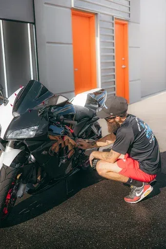 Man crouches next to a black and white motorcycle; orange doors in the background.