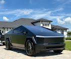 Tesla Cybertruck parked in front of a modern house on a sunny day.