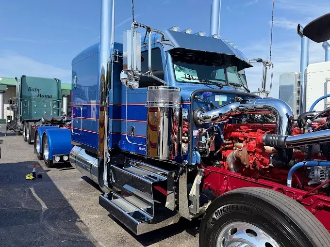 Blue and chrome semi-truck with open engine bay, parked outdoors on a sunny day.