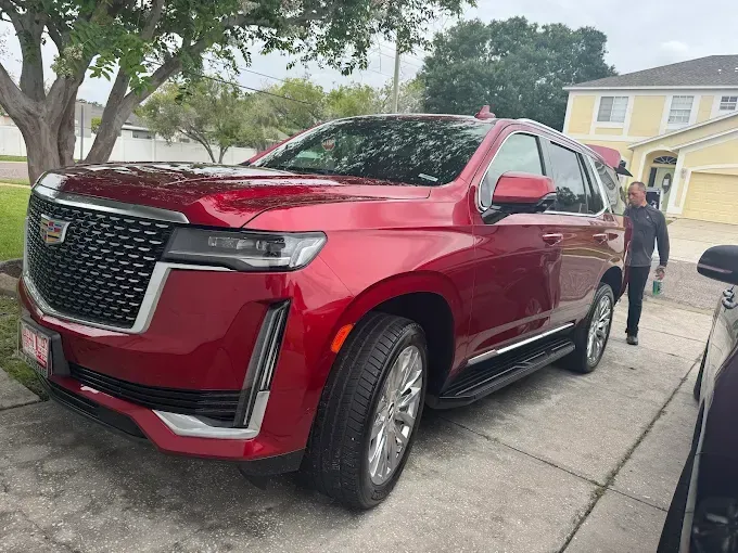 Red Cadillac Escalade SUV parked in a driveway; a person walks near the vehicle.
