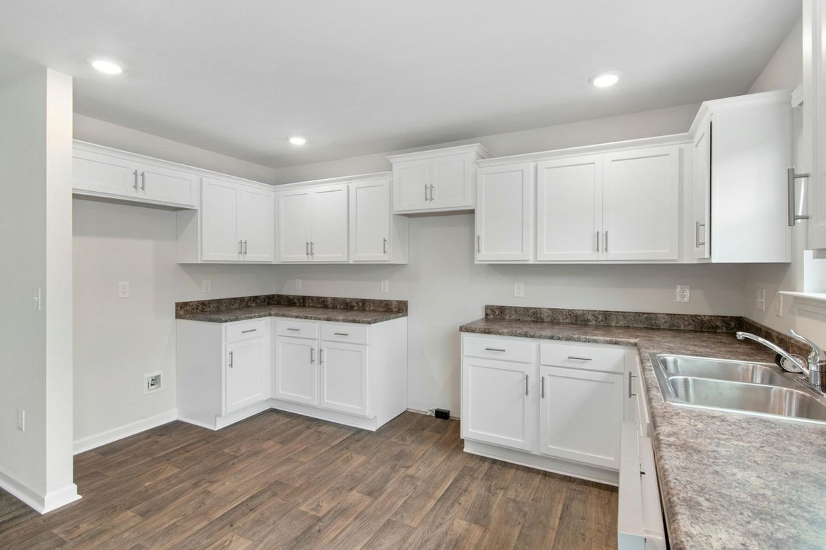 An empty kitchen with white cabinets and granite counter tops.