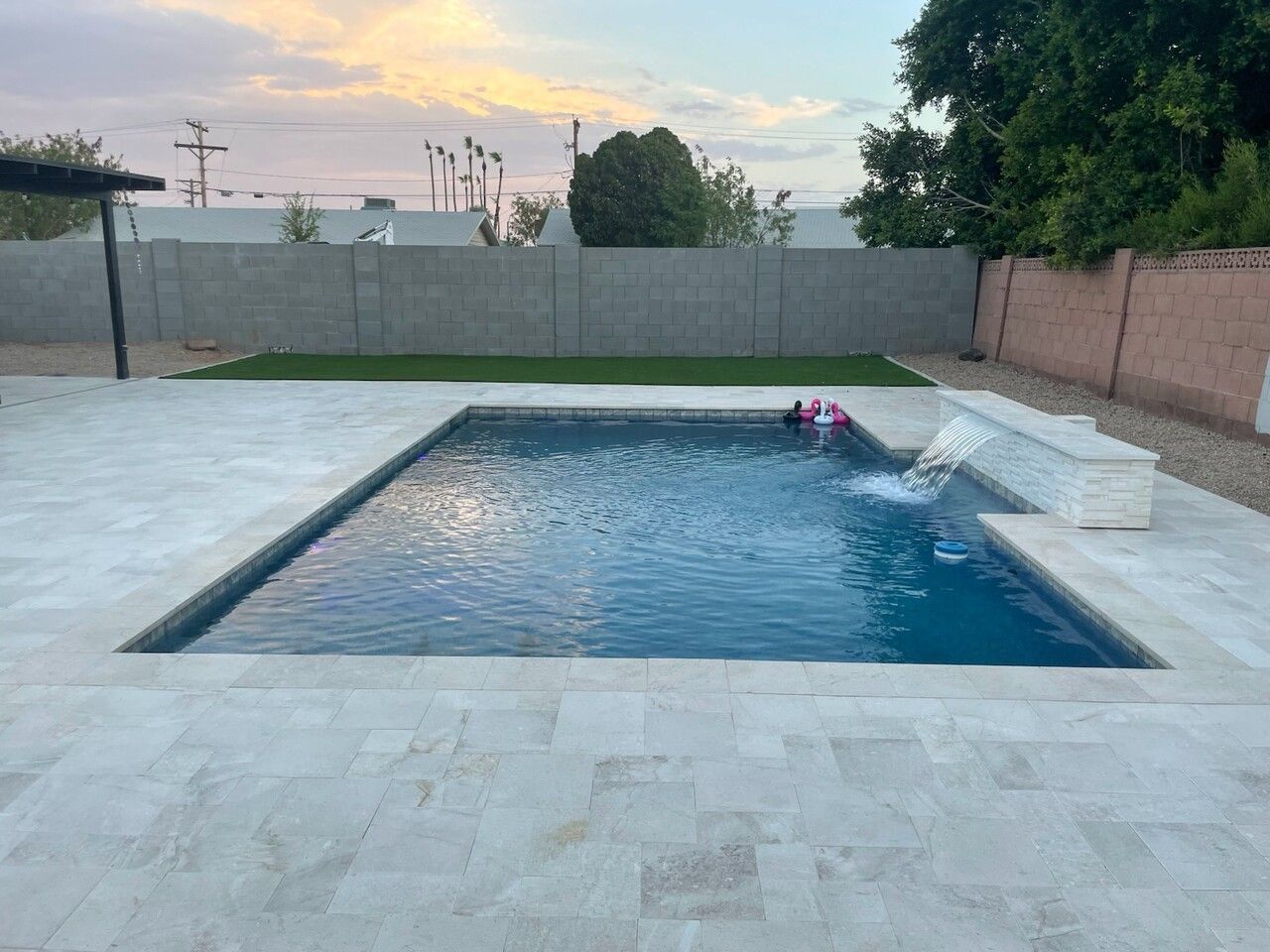 A large swimming pool with a waterfall in the backyard of a house.