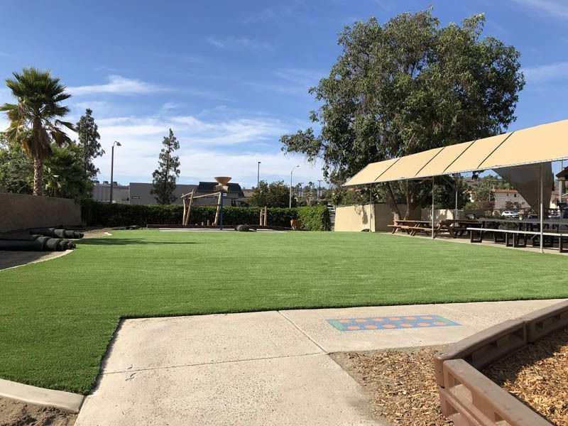 A large grassy field with a picnic table and umbrellas in the background