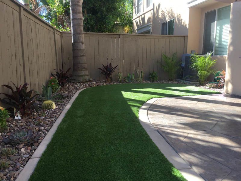 A backyard with a wooden fence and a synthetic grass lawn
