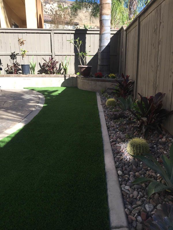 A backyard with a fence , grass , plants and rocks
