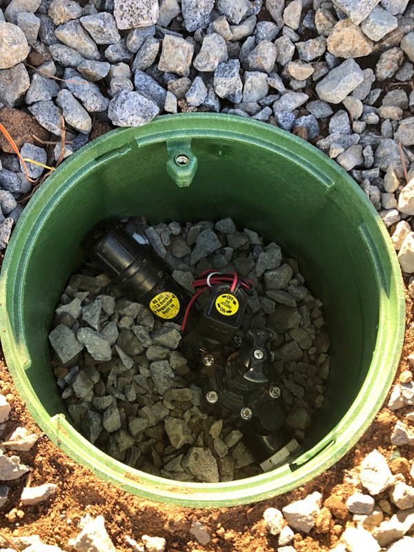 A green bucket filled with rocks and a sprinkler inside of it