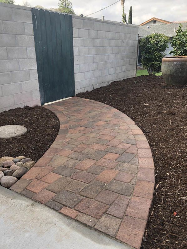 A brick walkway leading to a fence in a backyard