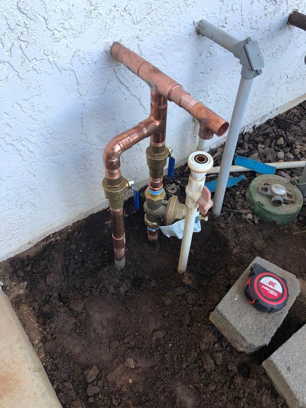 A copper pipe is sitting in the dirt next to a tape measure