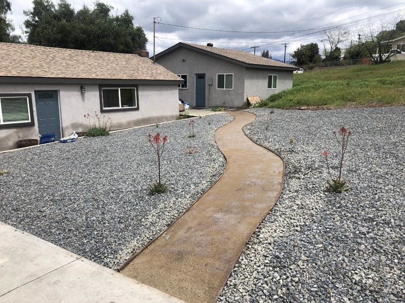 A concrete walkway leading to a house surrounded by gravel