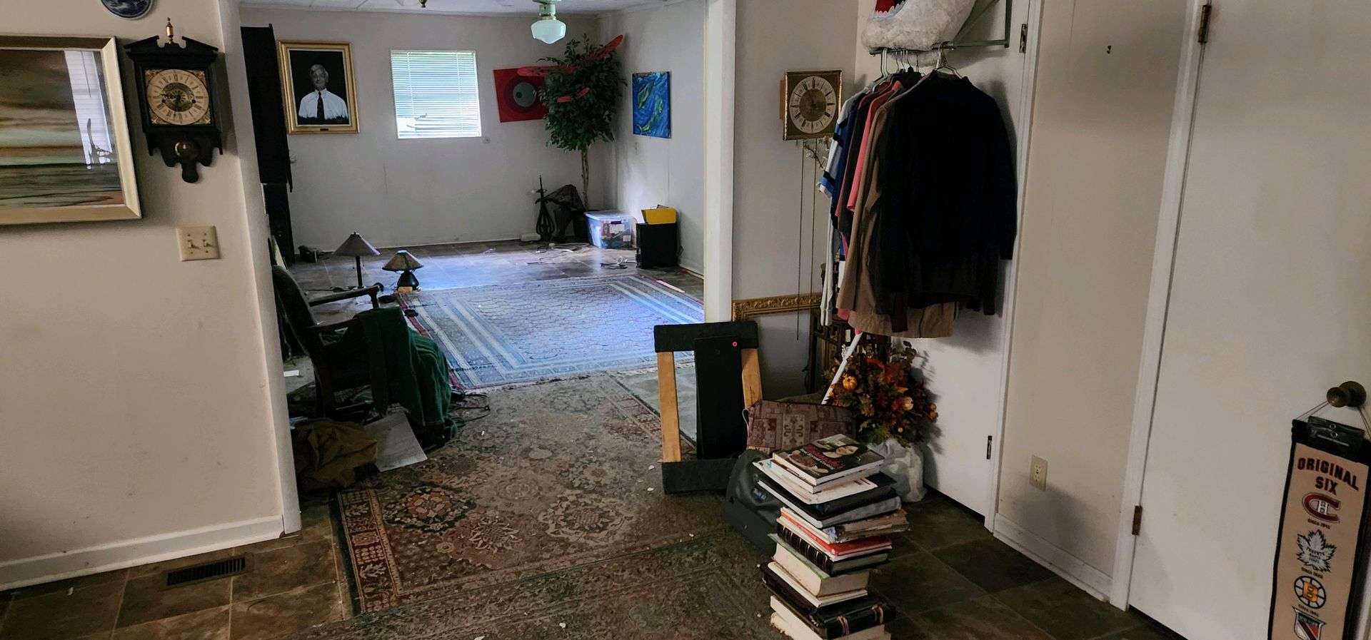 An interior view of a room with a rug, a rack of clothes, a stack of books, and various decorations.