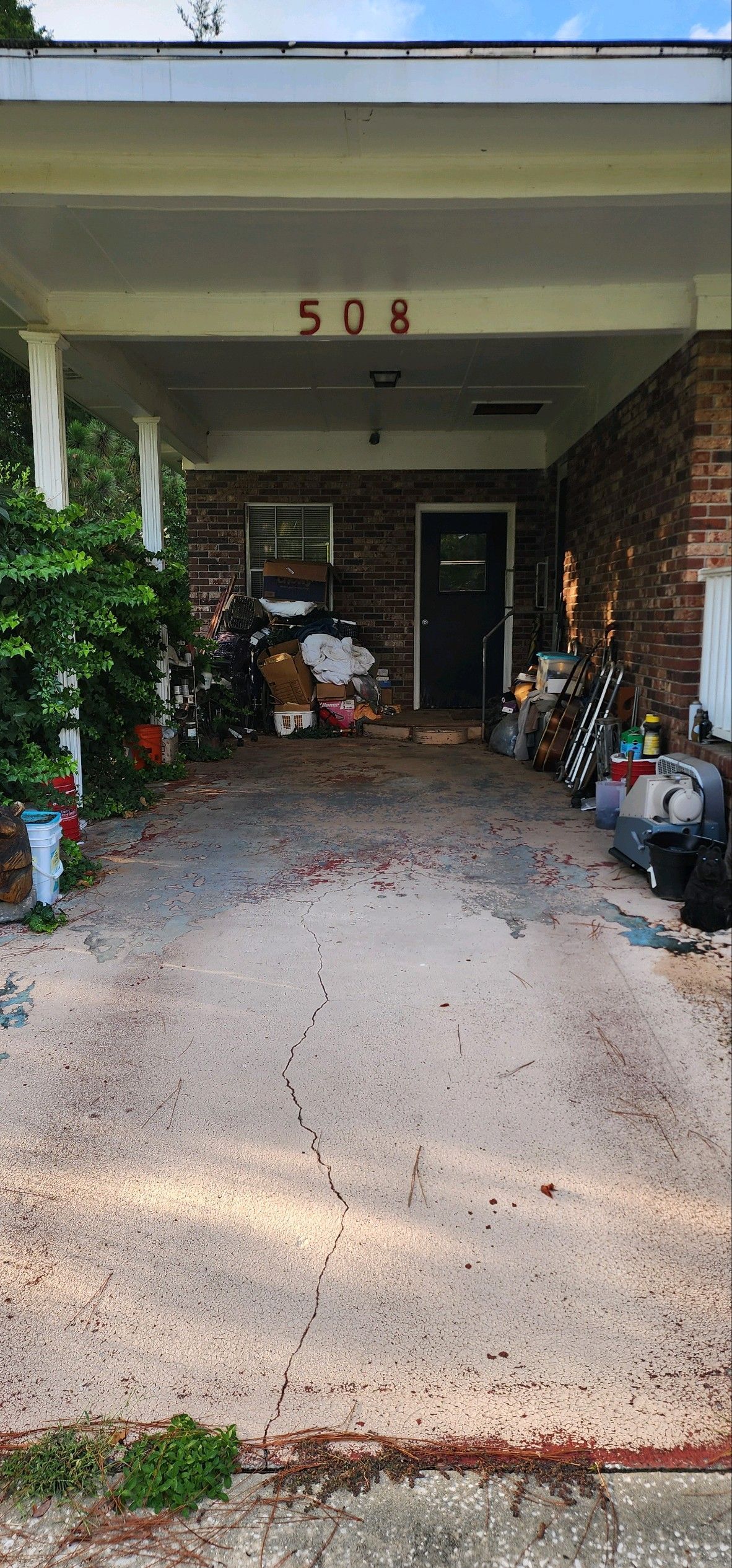 A cluttered driveway with debris and trash, leading to a house with the number 508 above the entrance.