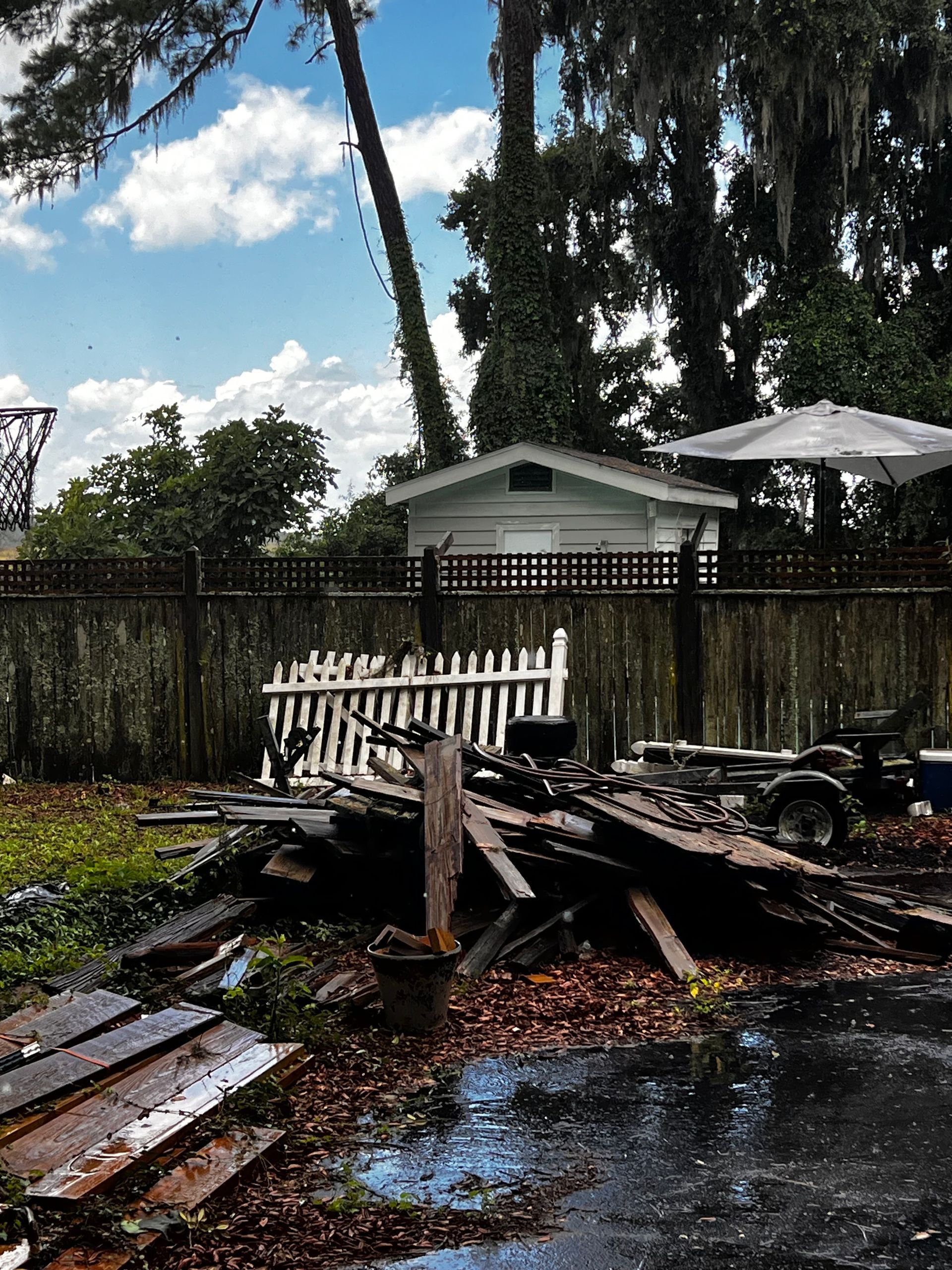Backyard scene: white picket fence, debris, small white building, and overcast sky.