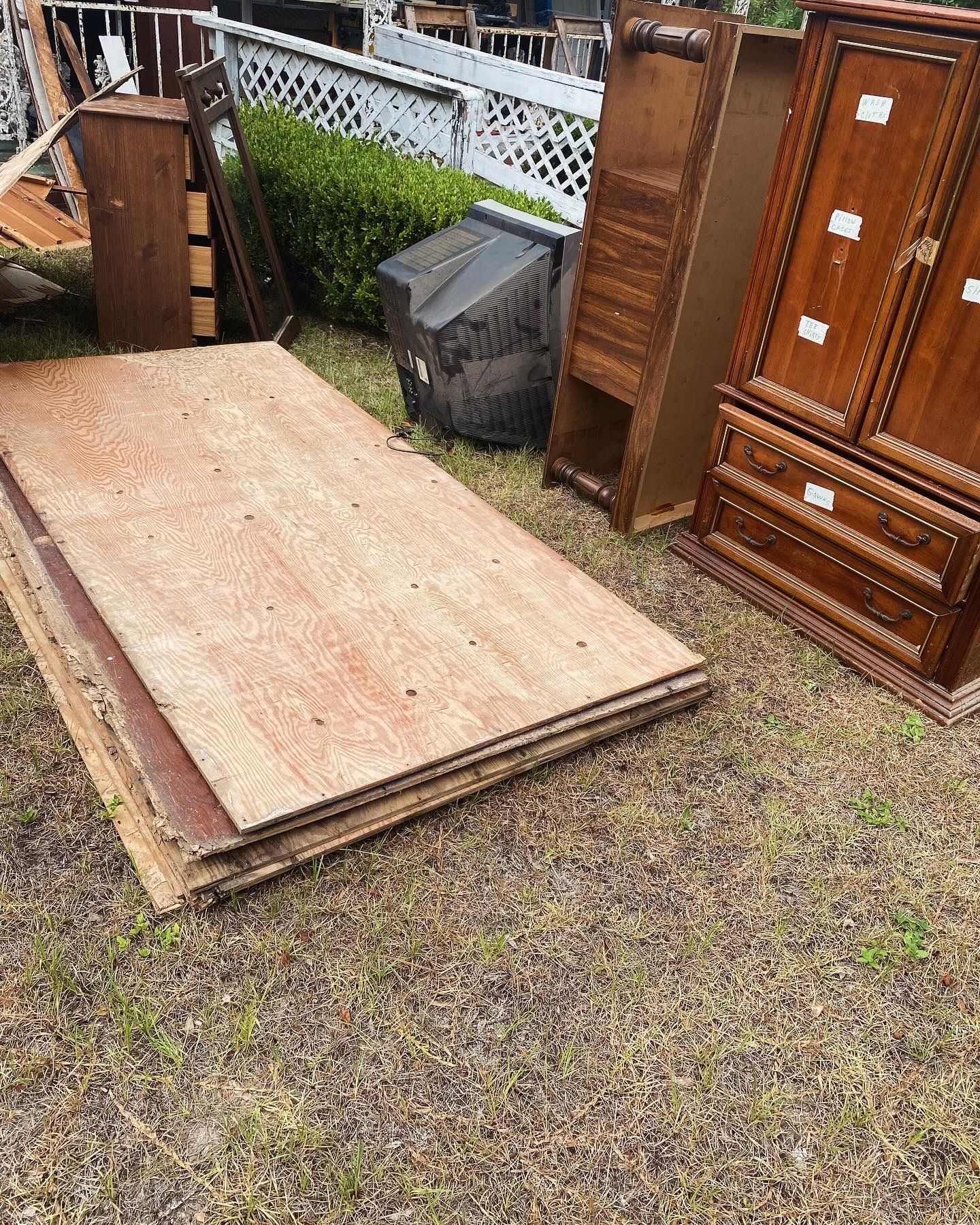 Pile of plywood and discarded furniture on grassy ground; includes a TV.