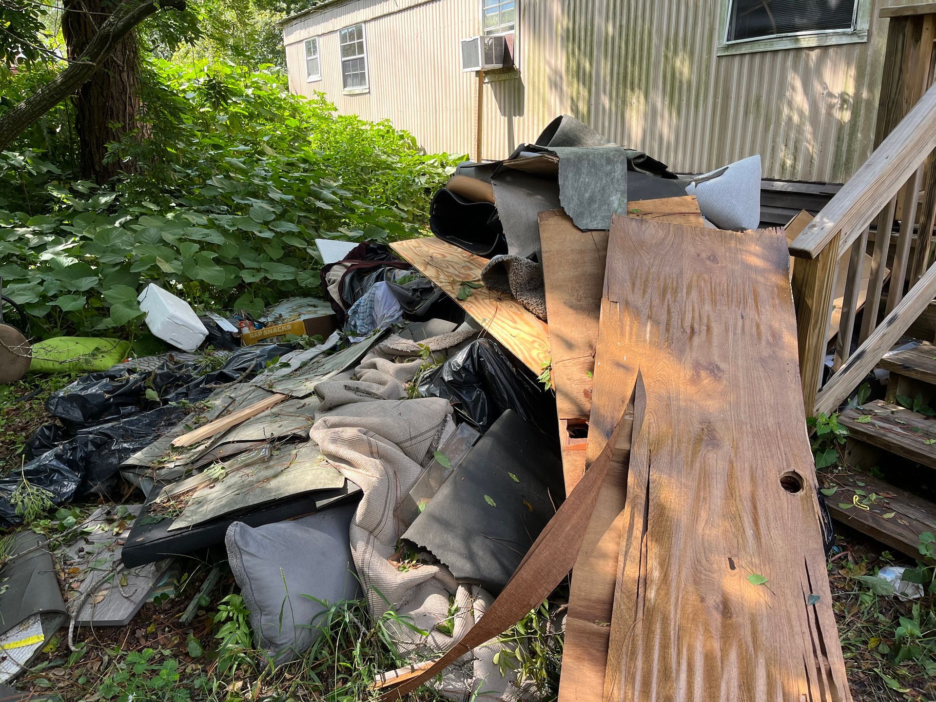 Pile of debris and trash near a weathered building and wooden steps; outdoors.