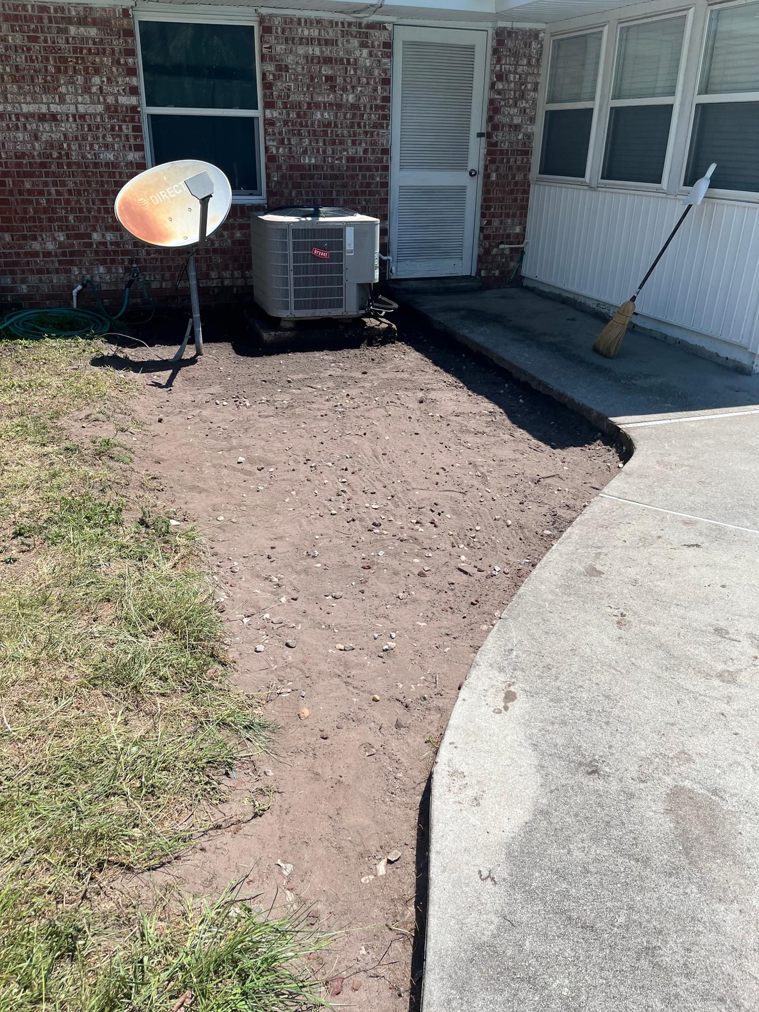 Bare dirt path next to a concrete sidewalk, leading to a brick building with an AC unit and a satellite dish.