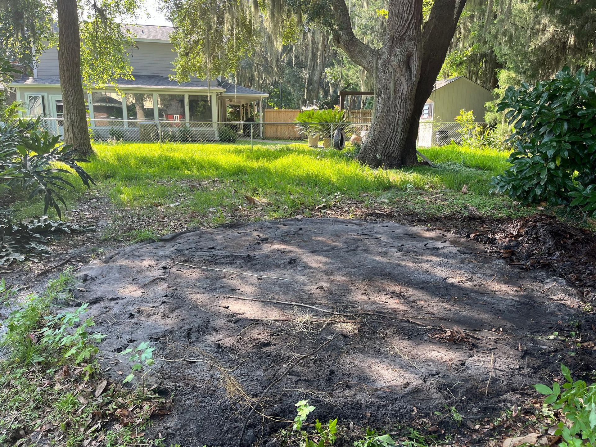 Pile of dark soil in grassy backyard, near trees and a house.
