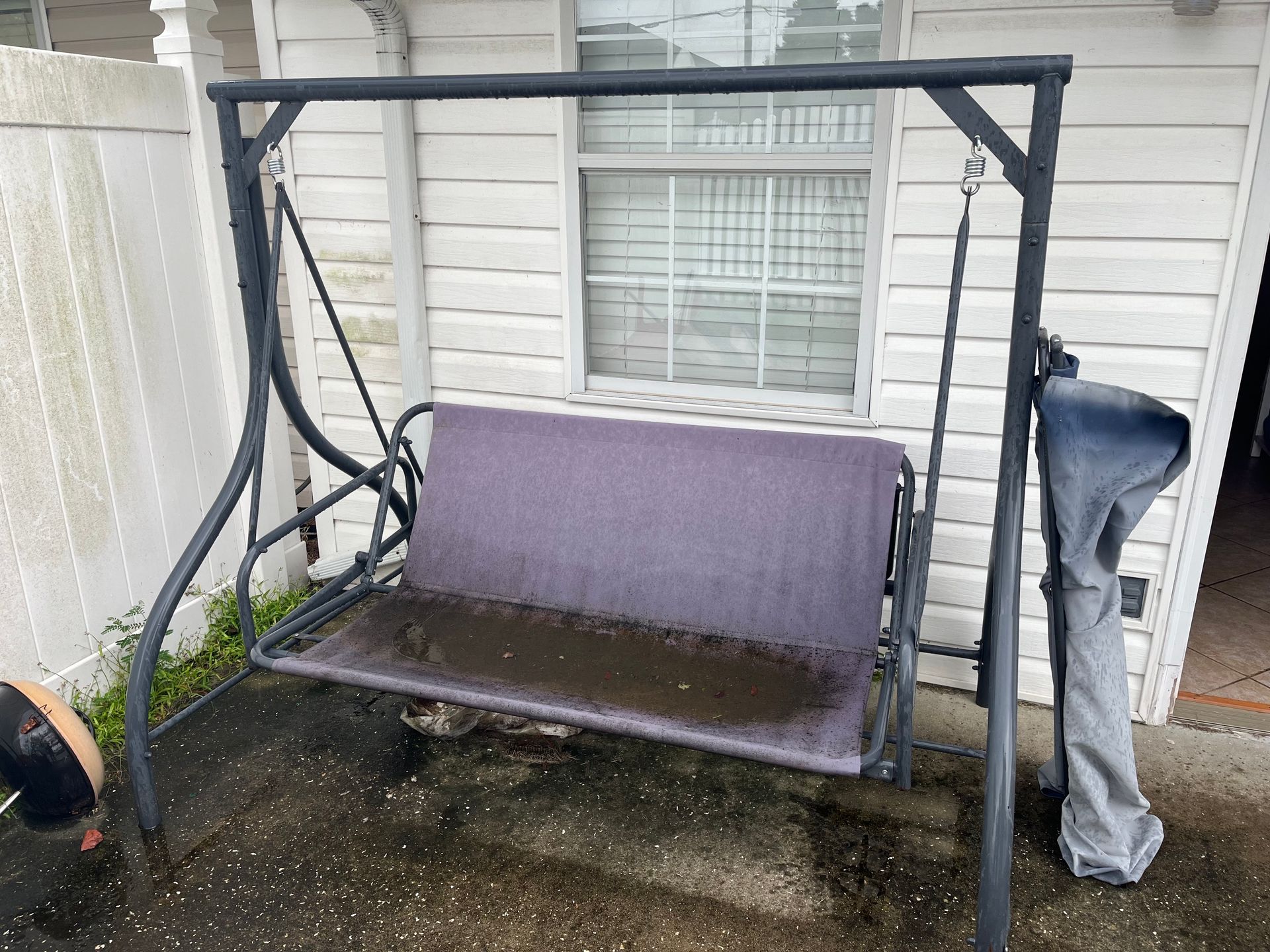 A black metal porch swing with purple seat sits outside. A gray cover hangs on the right side.