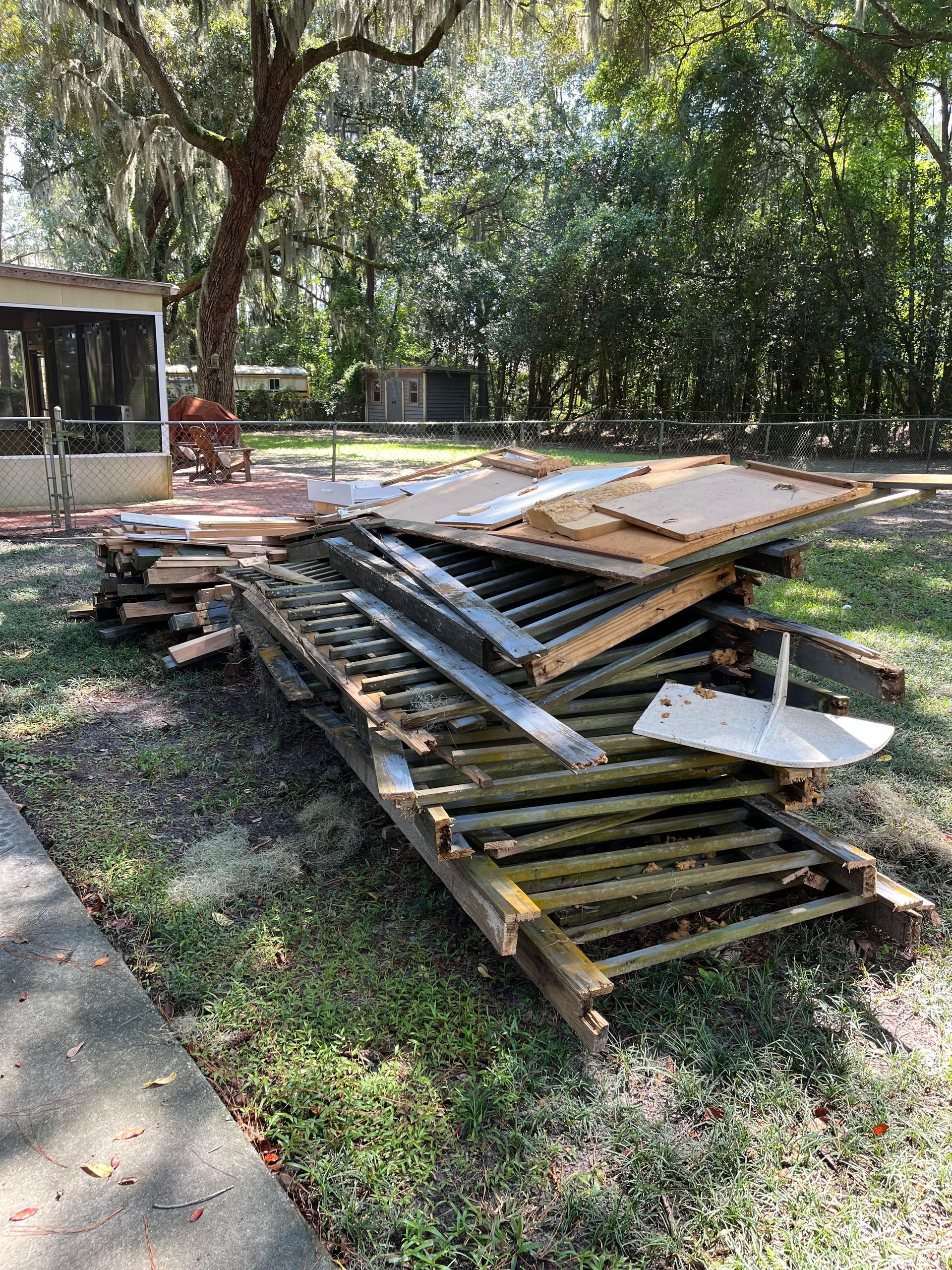 Pile of discarded wooden fence parts and debris on a grassy lawn in a backyard setting.