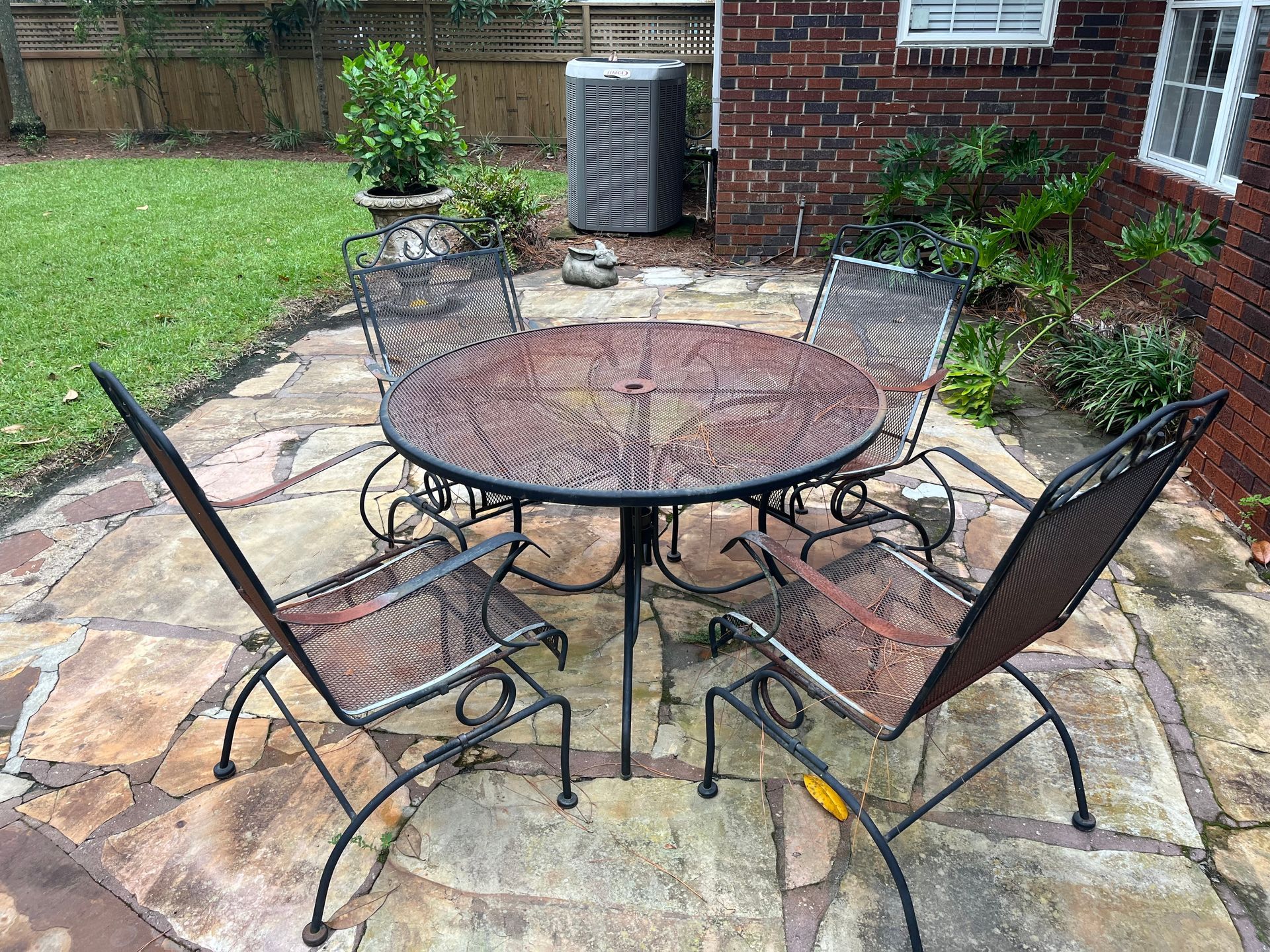 Metal patio table and chairs on a stone patio next to a brick house with a green lawn.