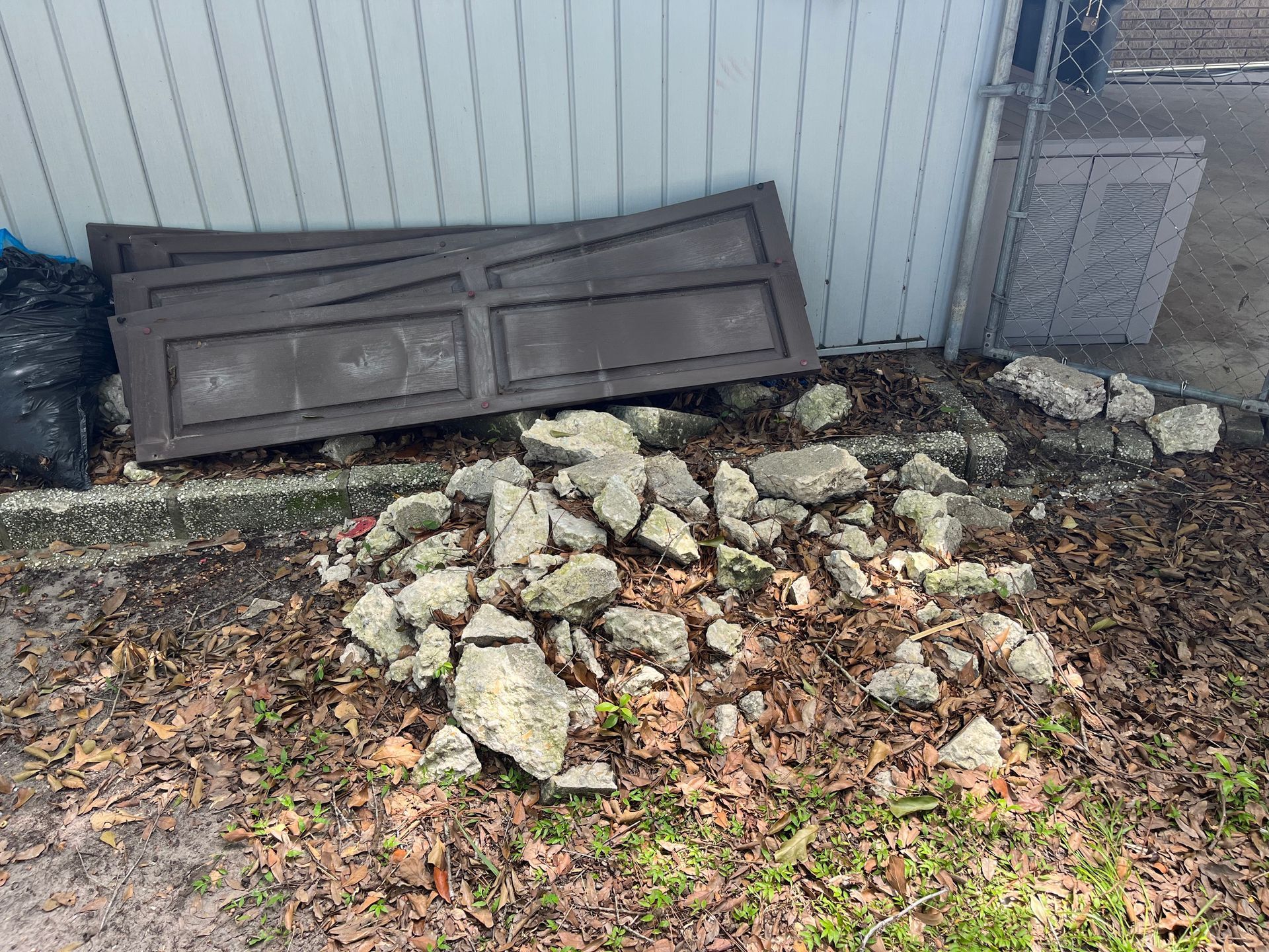 Pile of broken concrete debris with brown wood door pieces and a black trash bag against a light blue wall.