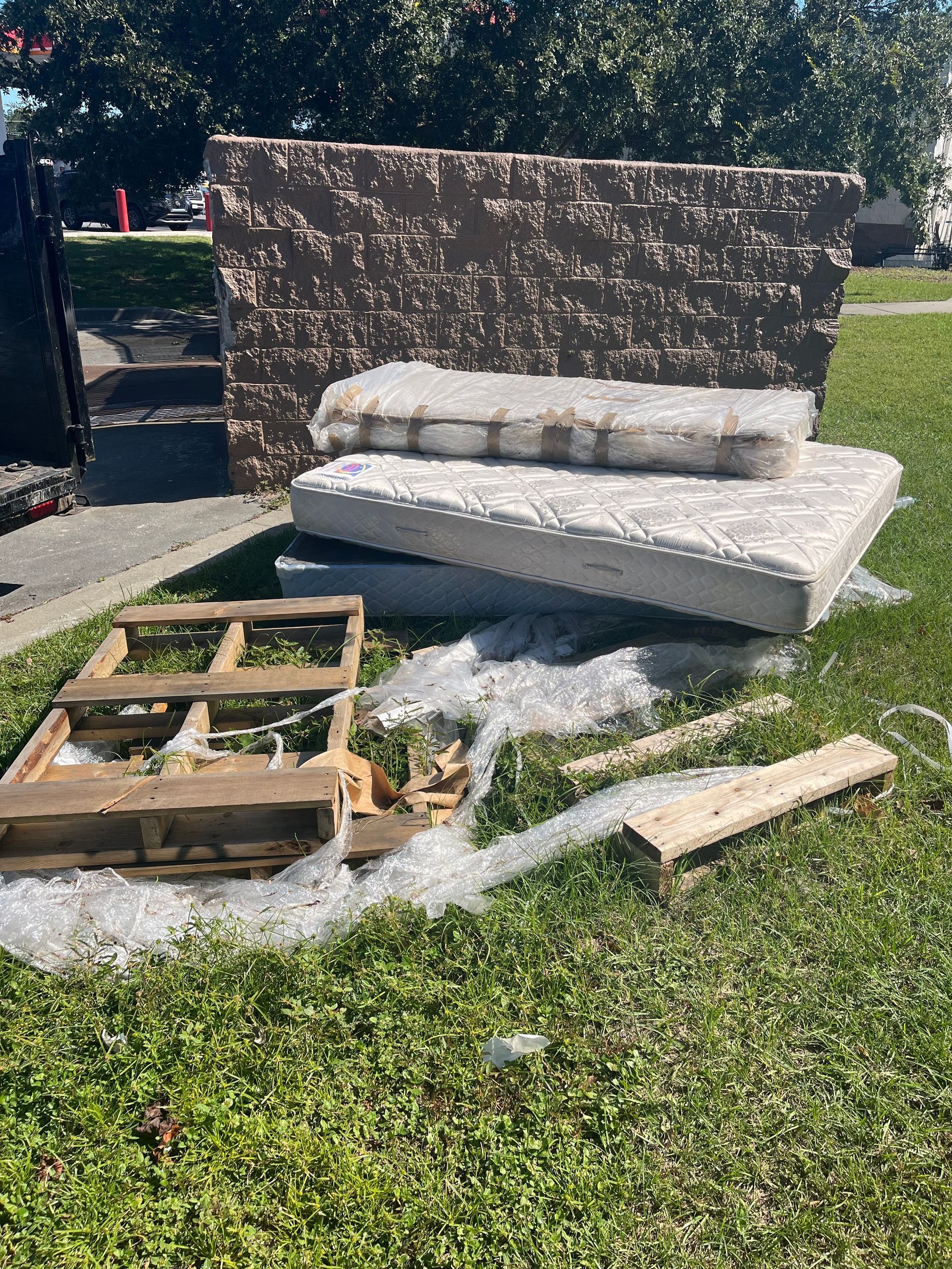 Mattresses, headboard, and pallet on a grassy lawn, awaiting trash pickup.