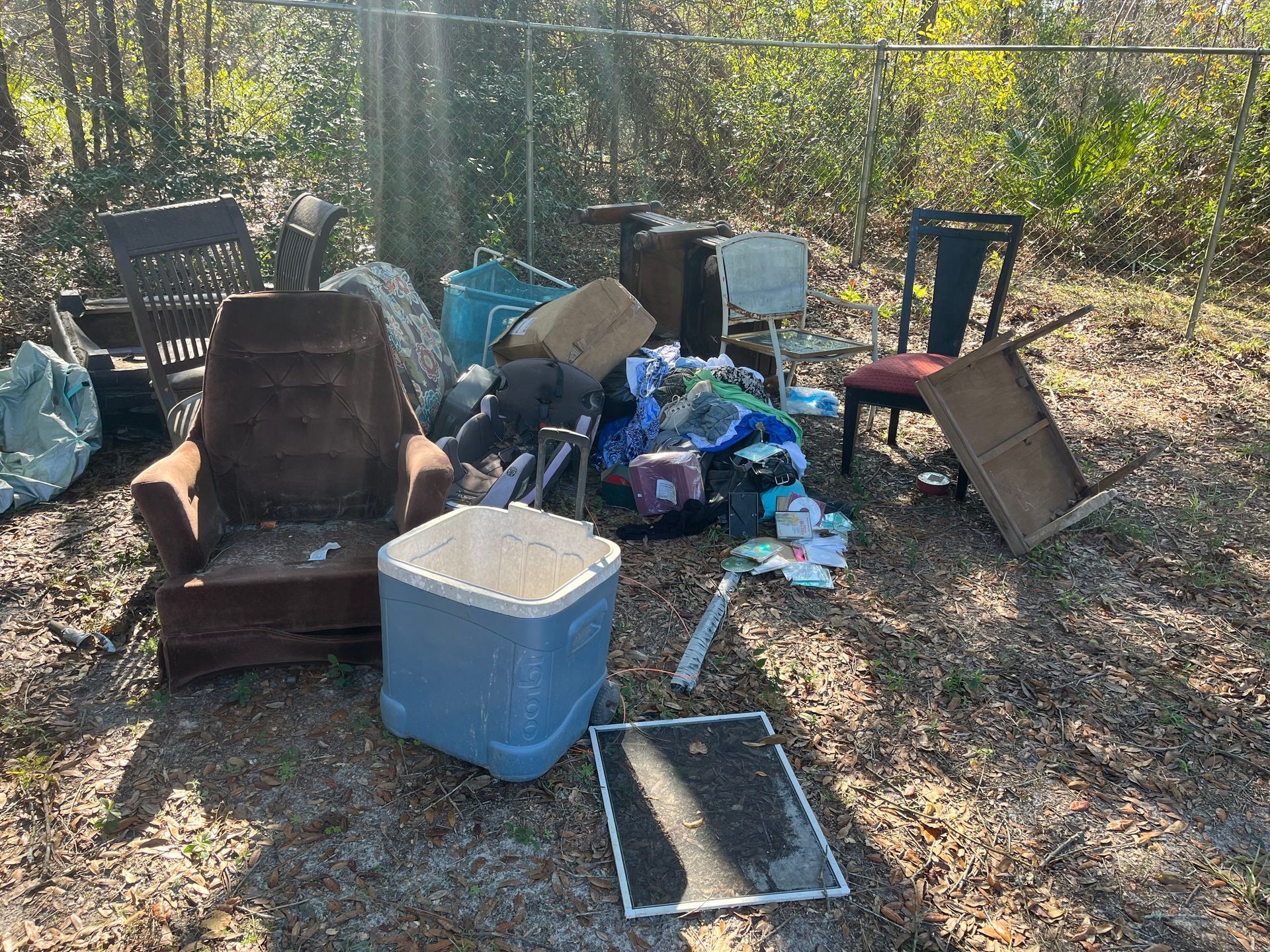 Pile of trash and discarded furniture outdoors. Includes chairs, an armchair, and an air cooler.
