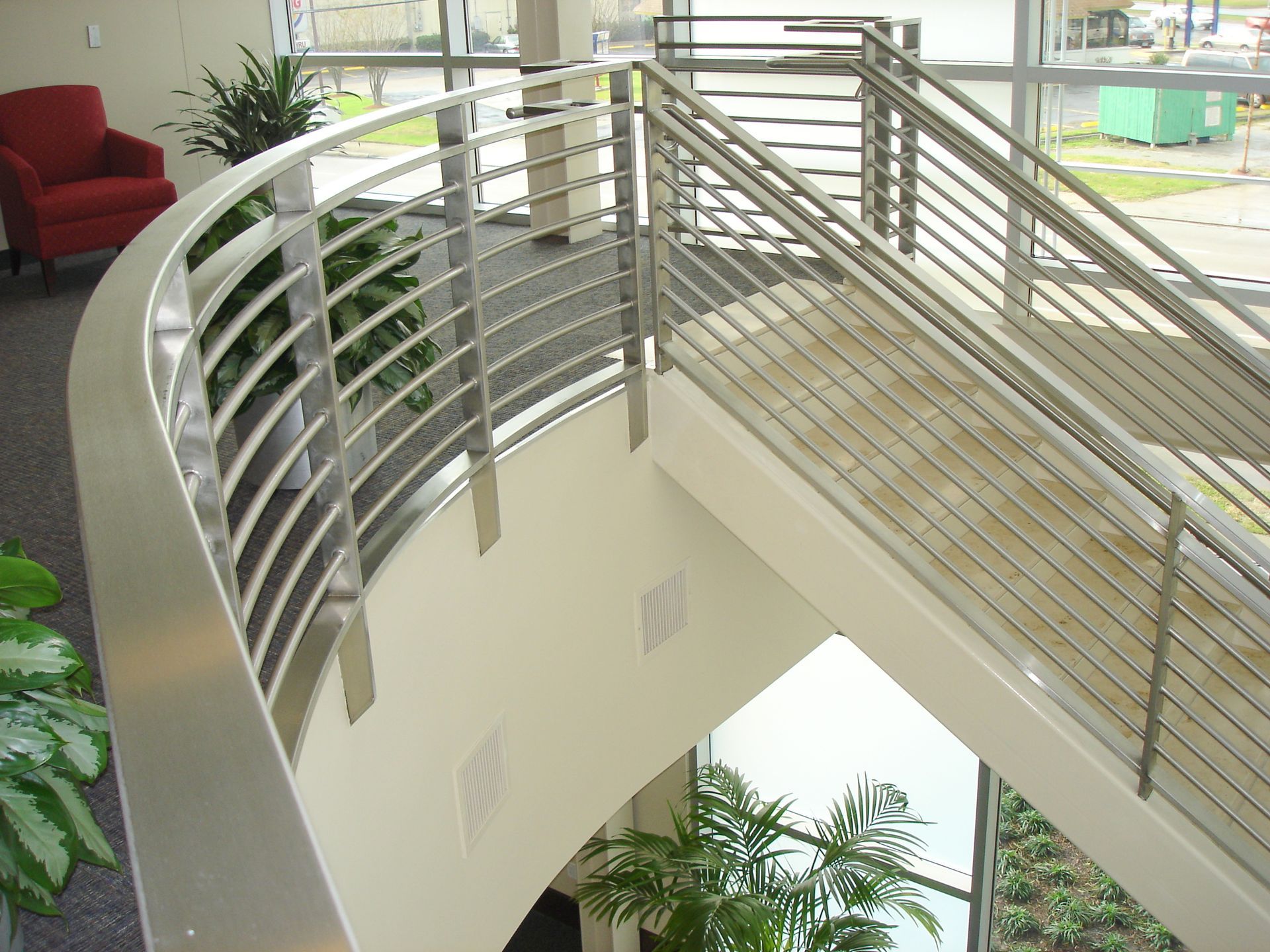 A staircase with a stainless steel railing and a red chair