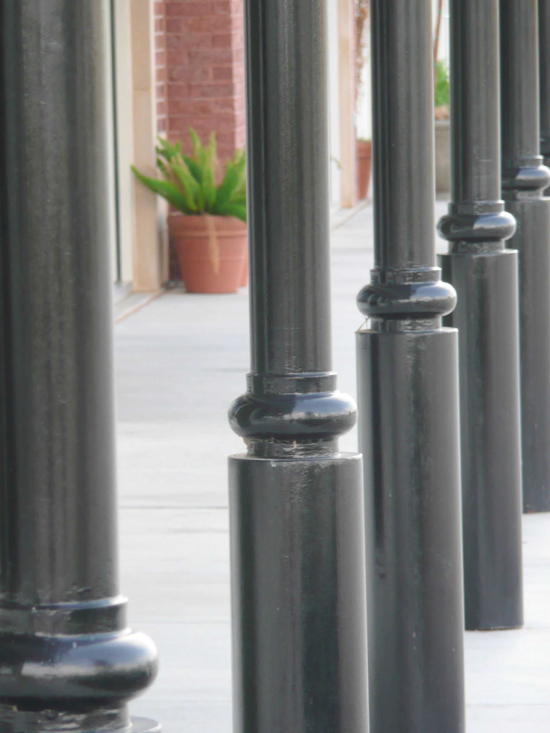 A row of black poles are lined up on a sidewalk.