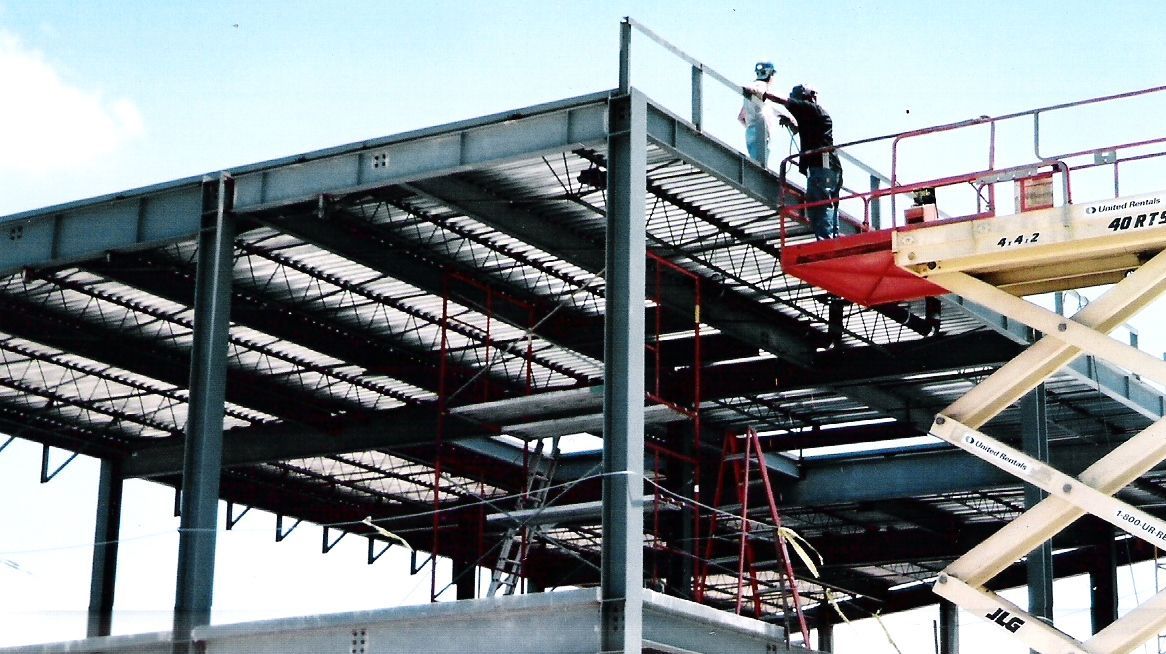 A man is standing on a scissor lift on top of a building under construction.