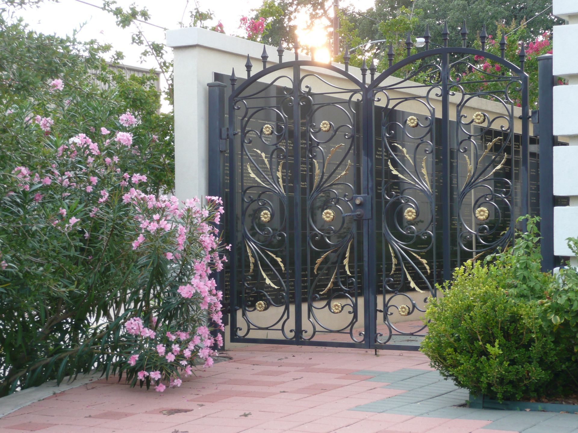 A wrought iron gate with pink flowers in front of it