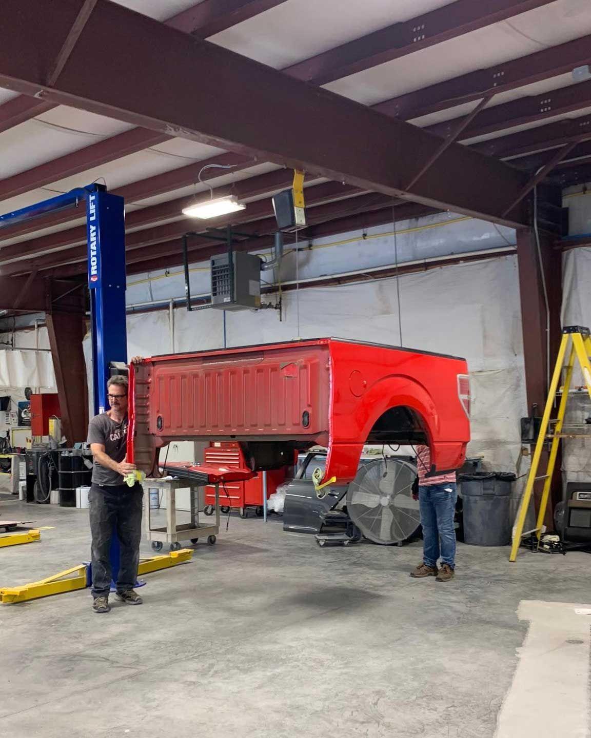 A man is standing next to a red truck in a garage.