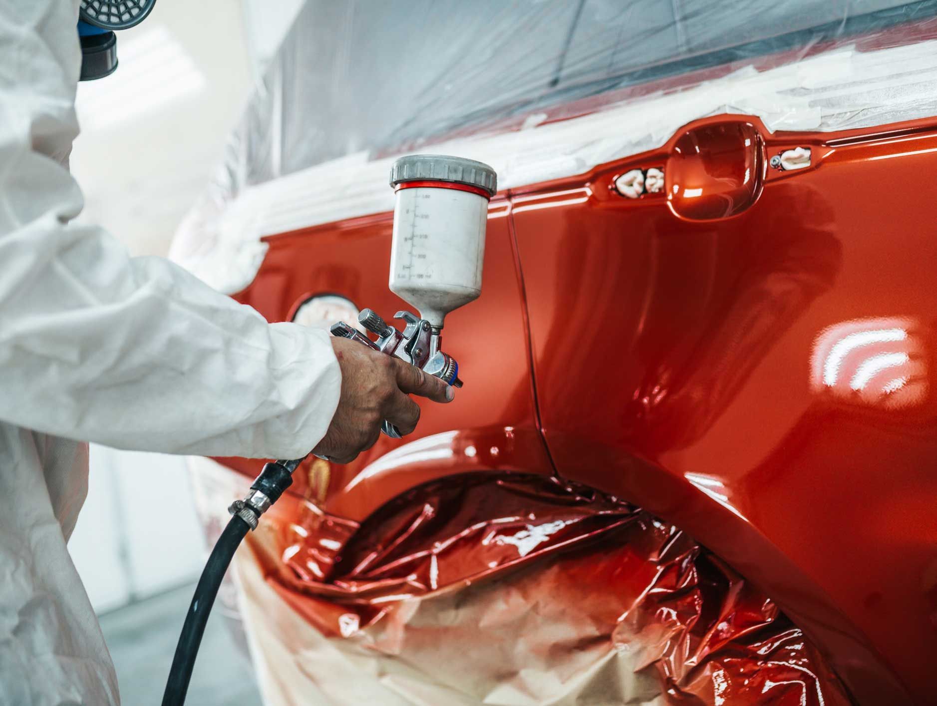 A man is spray painting a red car in a garage.
