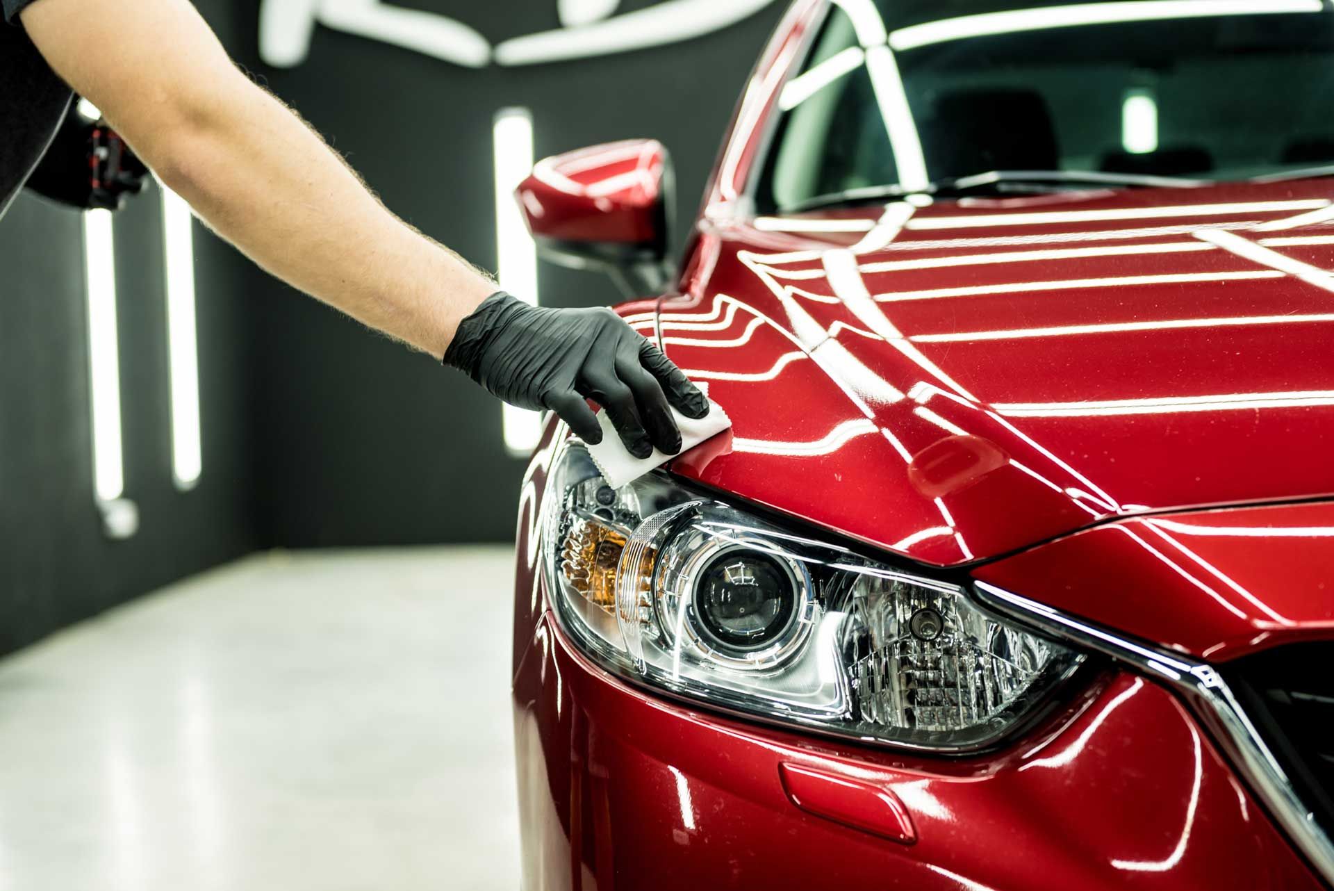 A person is polishing the hood of a red car.