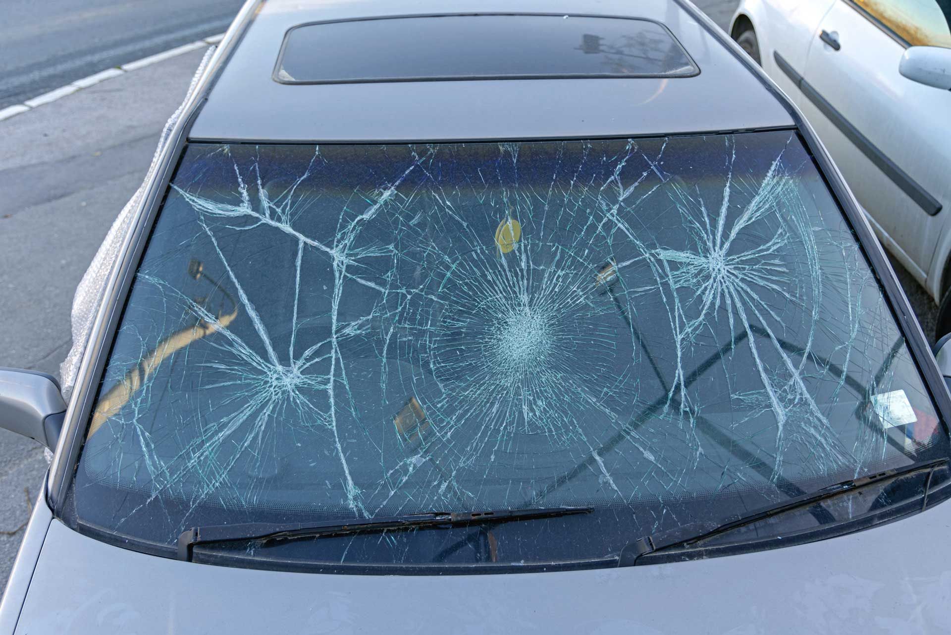 A car with a broken windshield is parked on the side of the road.