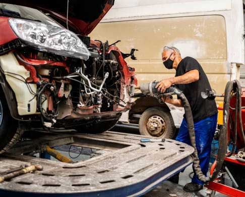 A man wearing a mask is working on a car in a garage.