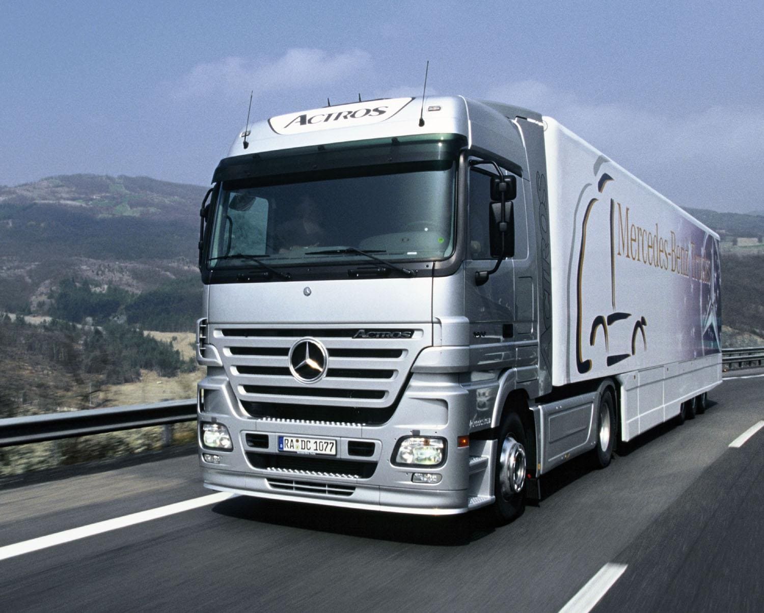 Ein silberner Mercedes Actros Sattelzug fährt auf einer Autobahn, im Hintergrund sind Berge zu sehen.