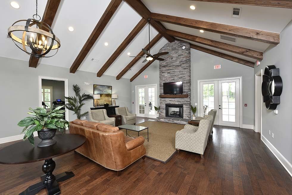 Lounge area with exposed beams, fireplace, leather sofa, and armchairs. Dark wood floors, gray walls, and natural light.
