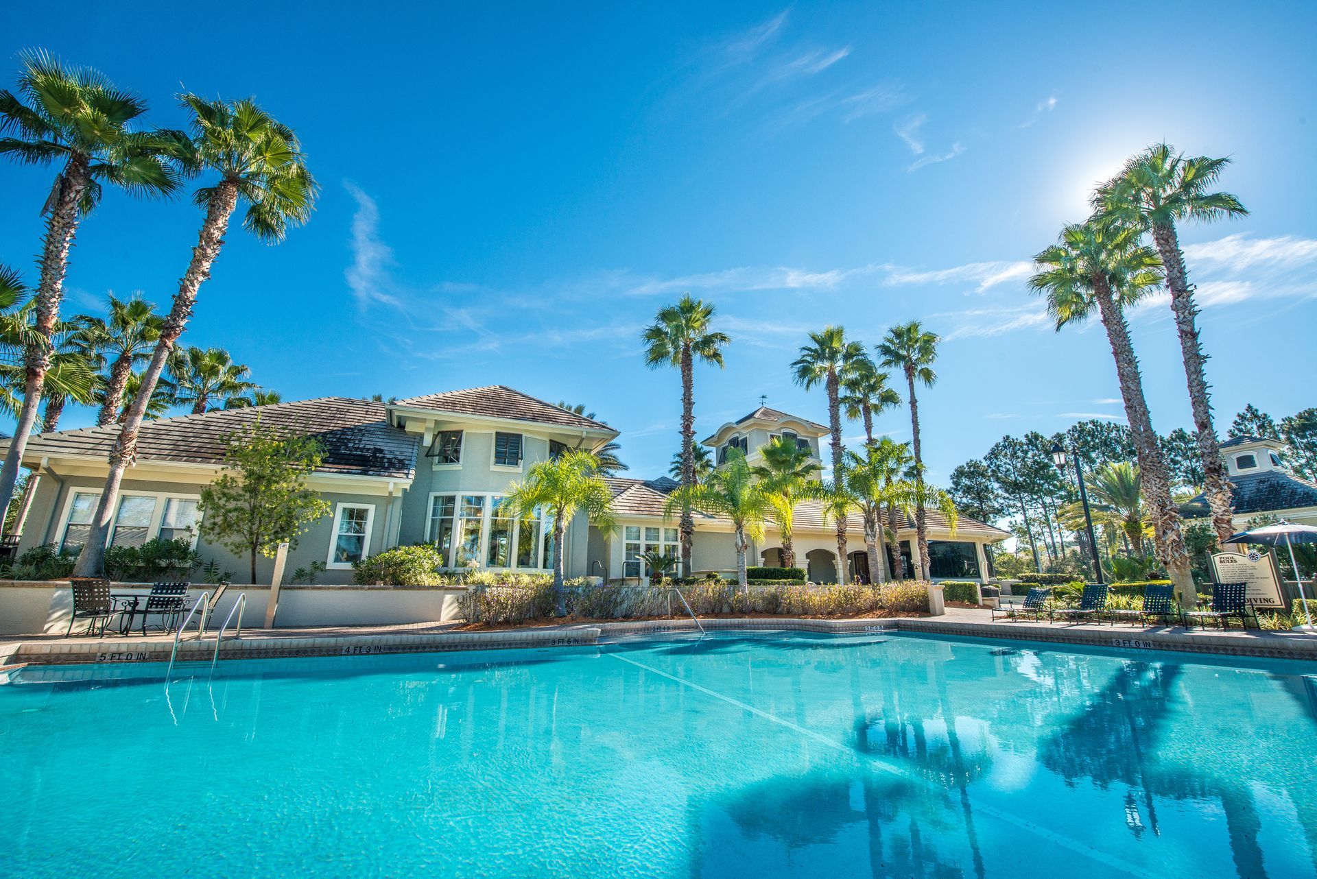 Swimming pool in front of a light blue building with palm trees under a bright blue sky.