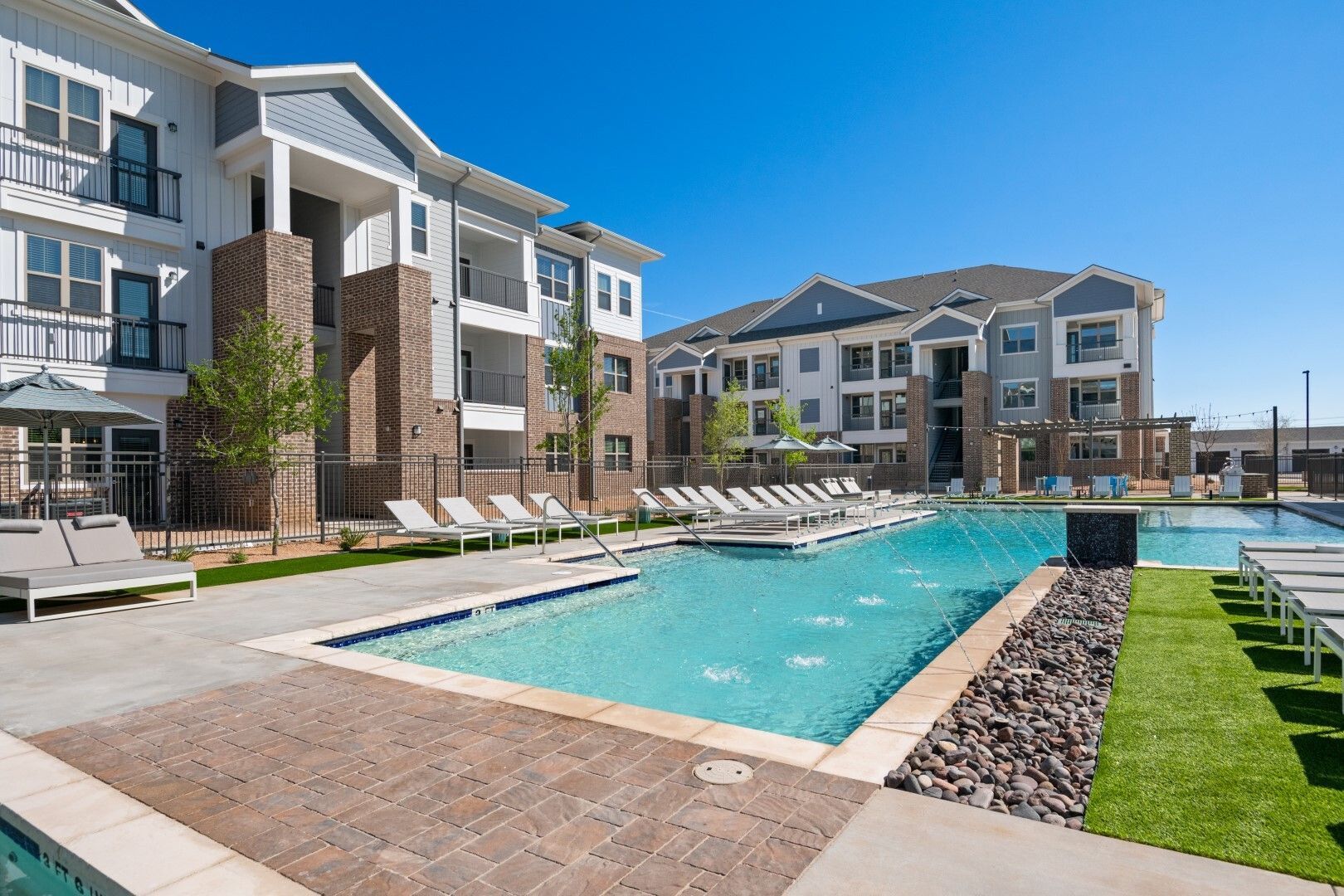 Apartment complex with a large pool, lounge chairs, and buildings with blue and white accents.