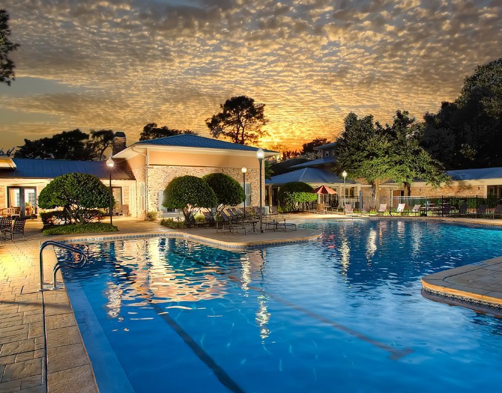 Swimming pool at dusk with a gazebo, trees, and sunset sky.