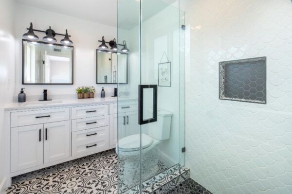 Bathroom with white cabinets, patterned floor, glass shower, and black accents.