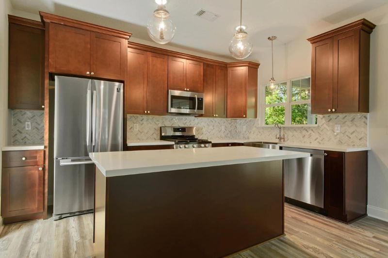 Modern kitchen with stainless steel appliances, brown cabinets, white countertops, and an island.