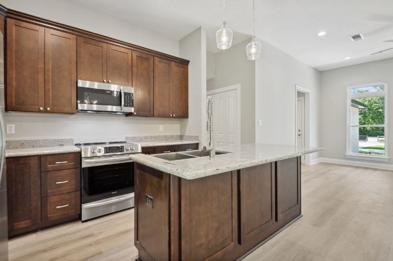 Kitchen with dark wood cabinets, stainless steel appliances, and a light granite countertop island.