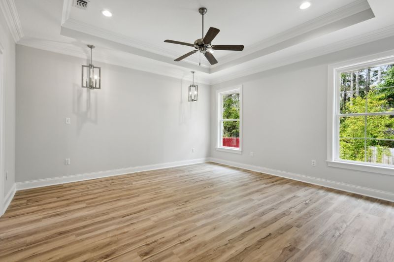 Empty room with wood floor, white walls, two windows, and a ceiling fan.